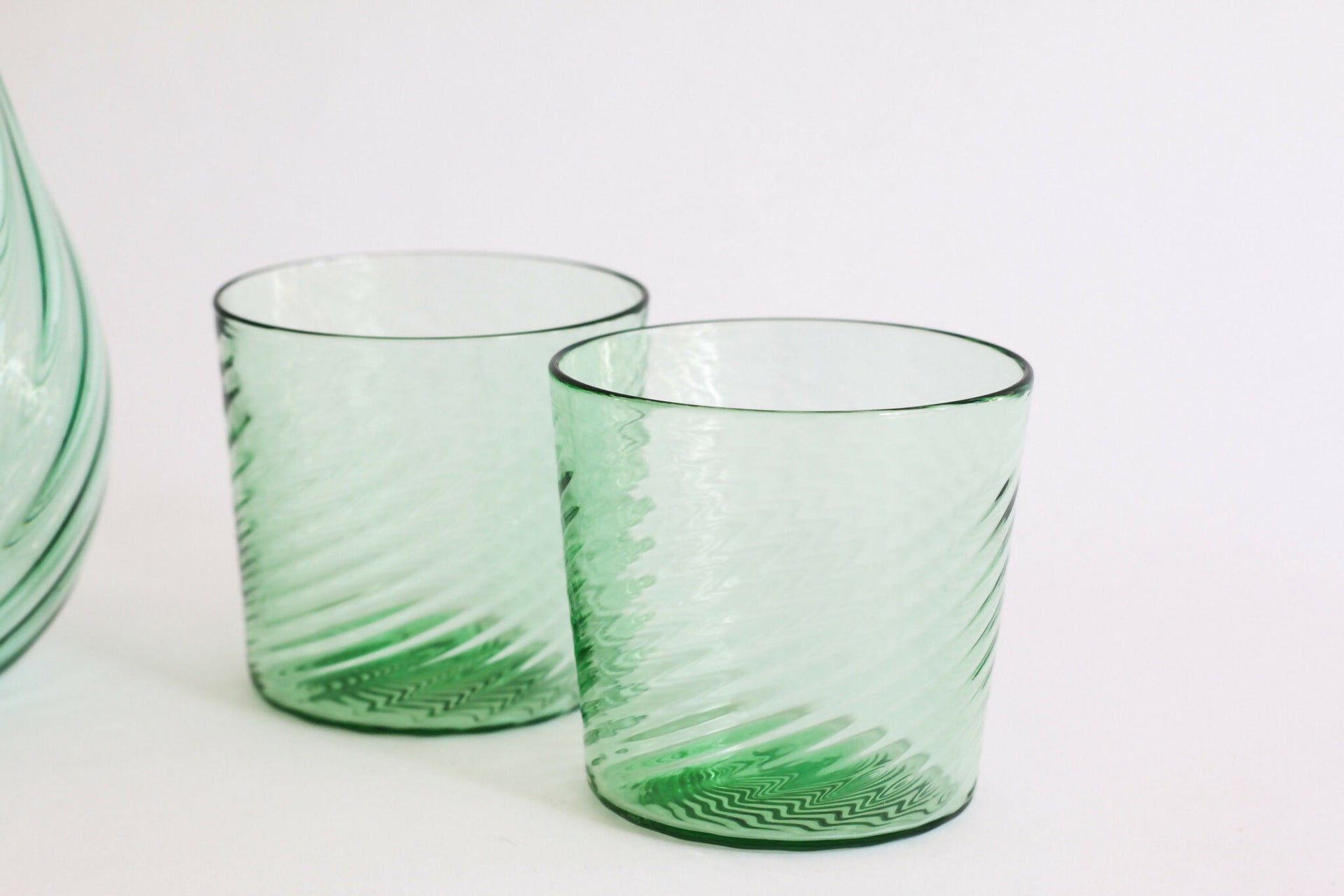 Two green glass tumblers with textured design on a white background,  available  to buy on the-salon.com. SALON curates the finest , unique, handmade pieces from the interior industry's best makers and brands. Shop luxury furniture, lighting, rugs, art, antiques and vintage pieces and accessories from SALON interior designed rooms.