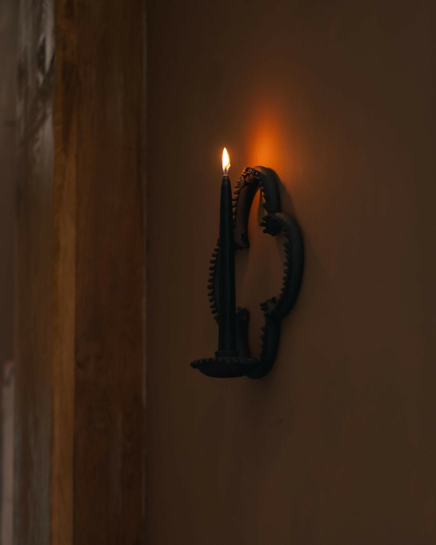 Wall-mounted candle holder with a lit candle on a plain wall,  available  to buy on the-salon.com. SALON curates the finest , unique, handmade pieces from the interior industry's best makers and brands. Shop luxury furniture, lighting, rugs, art, antiques and vintage pieces and accessories from SALON interior designed rooms.