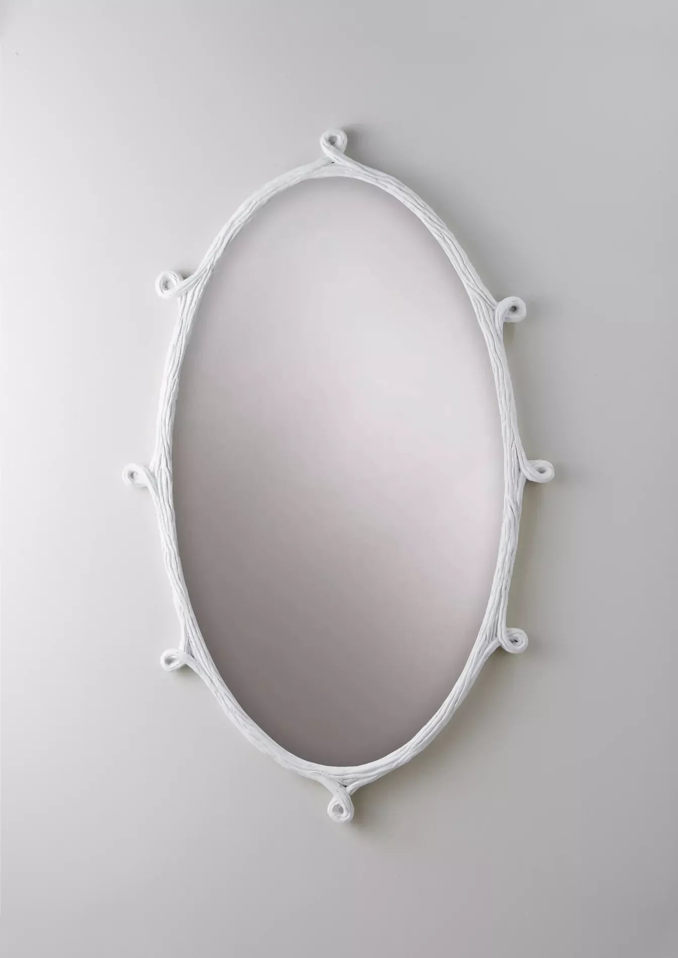Decorative oval mirror with a white wisteria frame on a light gray background, available  to buy on the-salon.com. SALON curates the finest , unique, handmade pieces from the interior industry's best makers and brands. Shop luxury furniture, lighting, rugs, art, antiques and vintage pieces and accessories from SALON interior designed rooms.