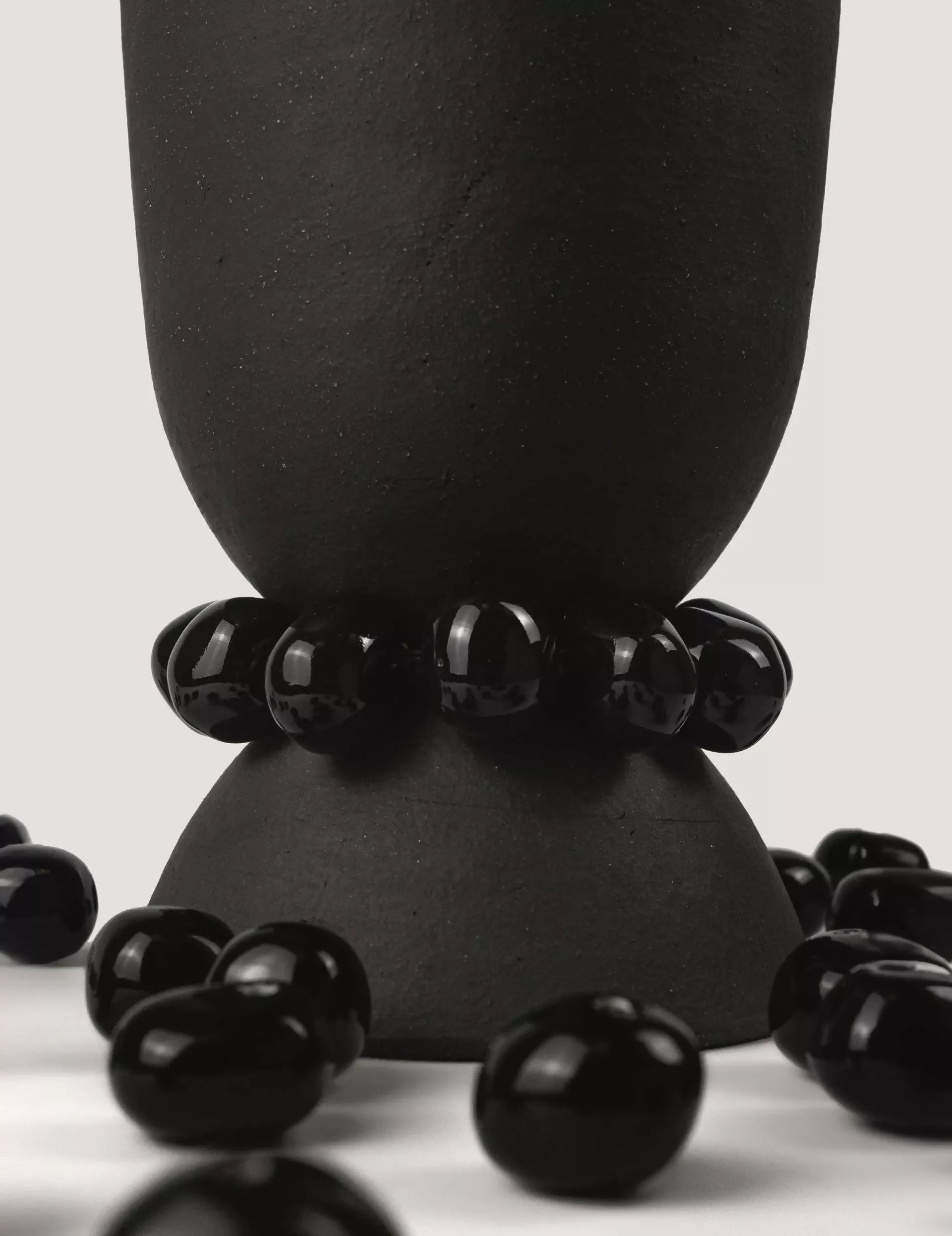 Black beaded bracelet on a black vase  with scattered beads on a light background, available  to buy on the-salon.com. SALON curates the finest , unique, handmade pieces from the interior industry's best makers and brands. Shop luxury furniture, lighting, rugs, art, antiques and vintage pieces and accessories from SALON interior designed rooms.