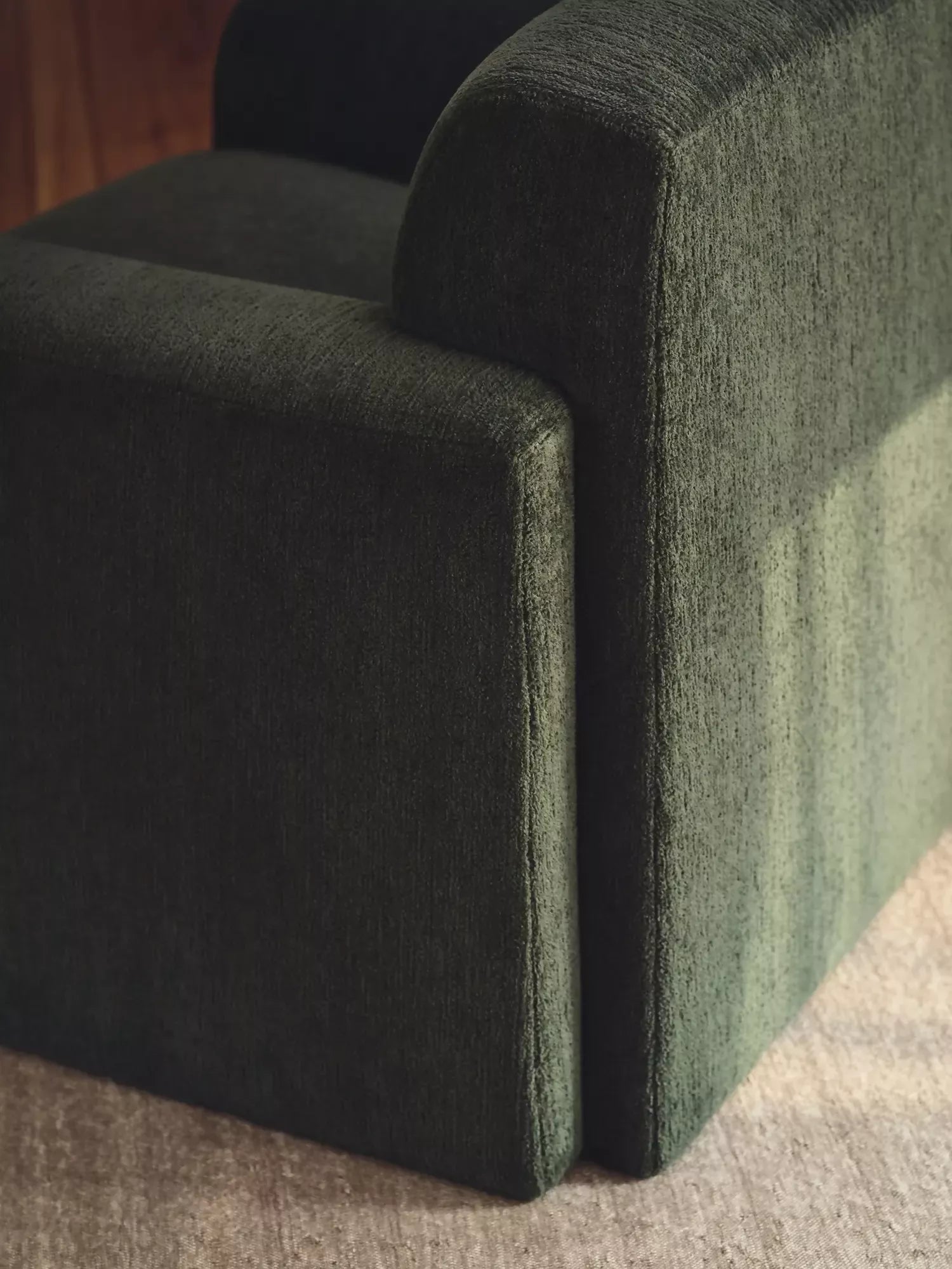 Close-up of a dark green upholstered chair corner on a textured surface, available  to buy on the-salon.com. SALON curates the finest , unique, handmade pieces from the interior industry's best makers and brands. Shop luxury furniture, lighting, rugs, art, antiques and vintage pieces and accessories from SALON interior designed rooms.