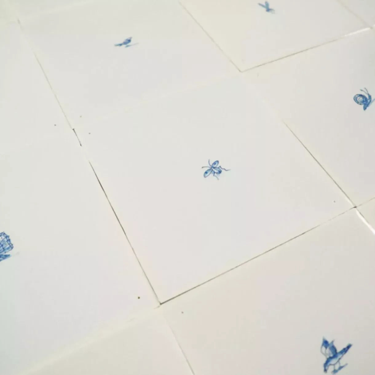 White tiles with blue butterfly designs on a white background,  available  to buy on the-salon.com. SALON curates the finest , unique, handmade pieces from the interior industry's best makers and brands. Shop luxury furniture, lighting, rugs, art, antiques and vintage pieces and accessories from SALON interior designed rooms.