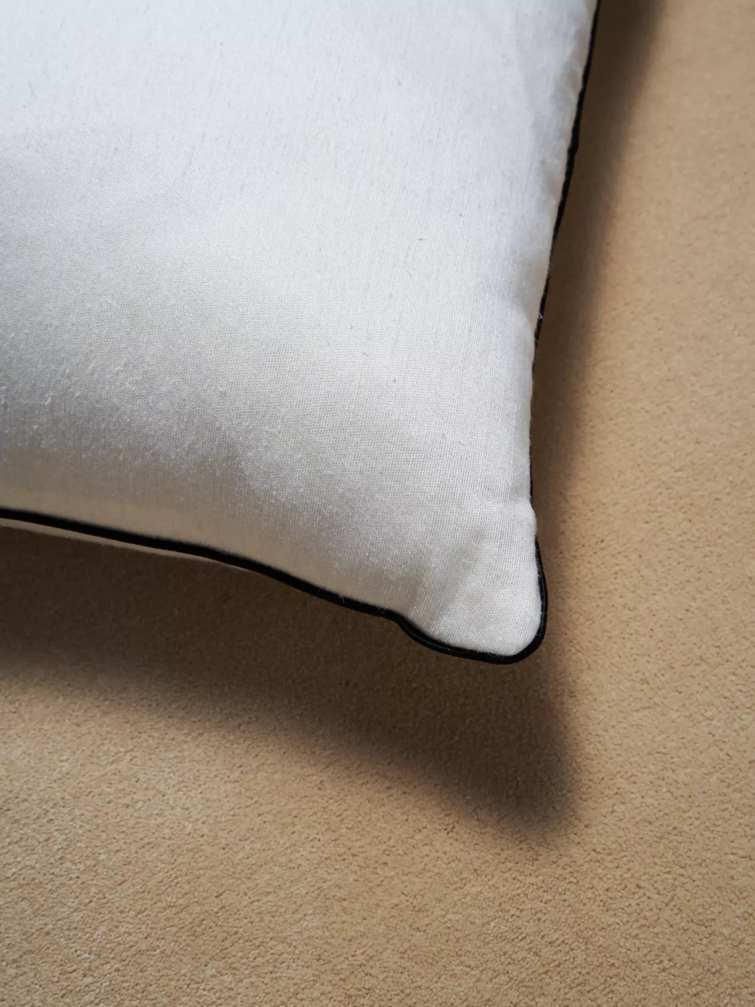 A close up of a white pillow and its black edges on a beige background,  available  to buy on the-salon.com. SALON curates the finest , unique, handmade pieces from the interior industry's best makers and brands. Shop luxury furniture, lighting, rugs, art, antiques and vintage pieces and accessories from SALON interior designed rooms.