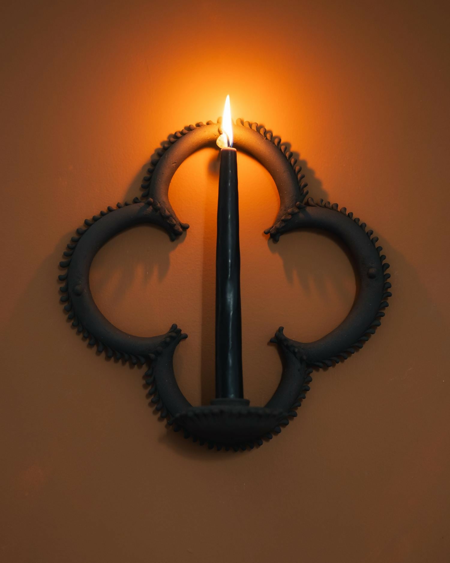 Decorative wall sconce with gears and a lit candle on a beige wall,  available  to buy on the-salon.com. SALON curates the finest , unique, handmade pieces from the interior industry's best makers and brands. Shop luxury furniture, lighting, rugs, art, antiques and vintage pieces and accessories from SALON interior designed rooms.