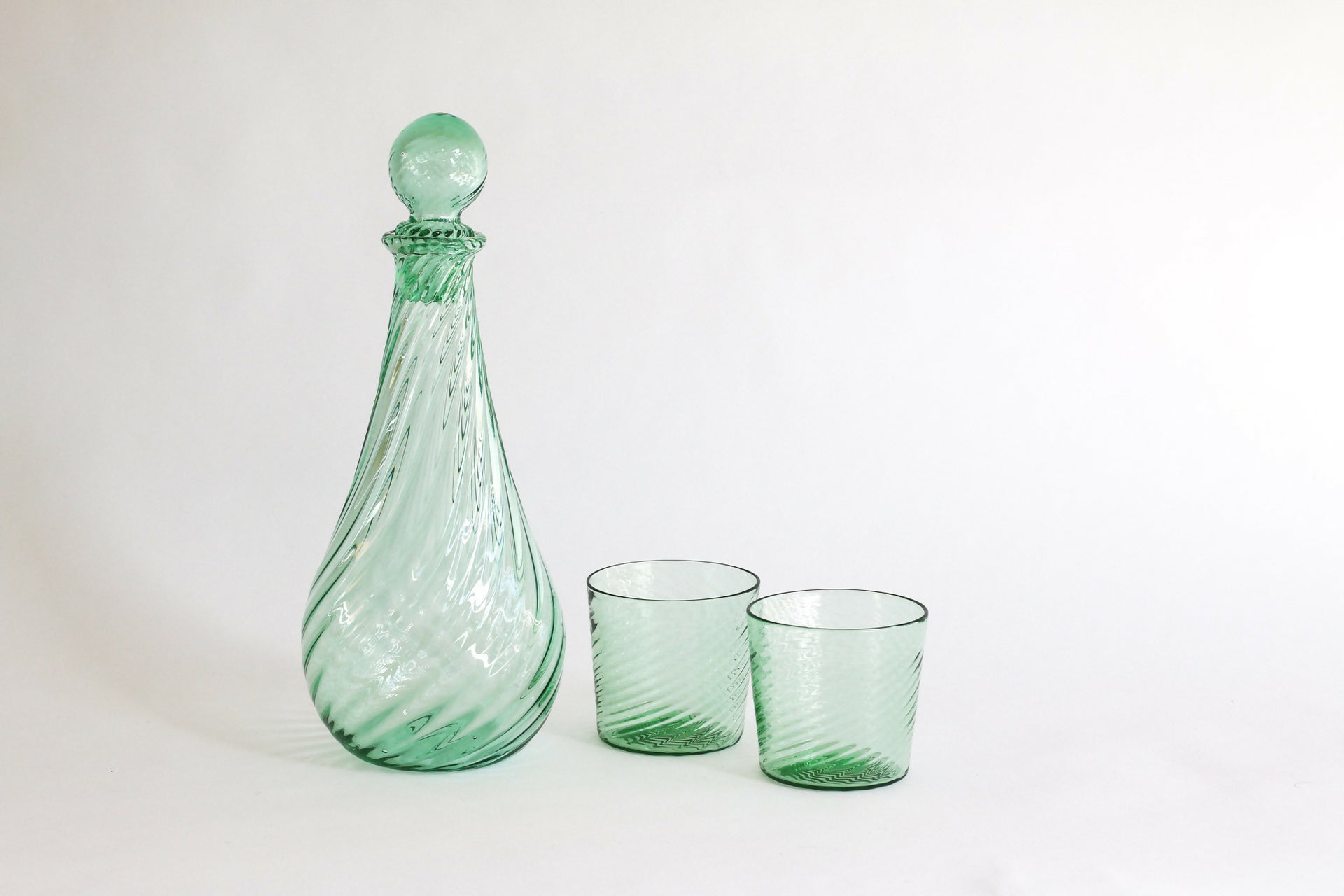 Green glass decanter and two glasses on a white background,  available  to buy on the-salon.com. SALON curates the finest , unique, handmade pieces from the interior industry's best makers and brands. Shop luxury furniture, lighting, rugs, art, antiques and vintage pieces and accessories from SALON interior designed rooms.