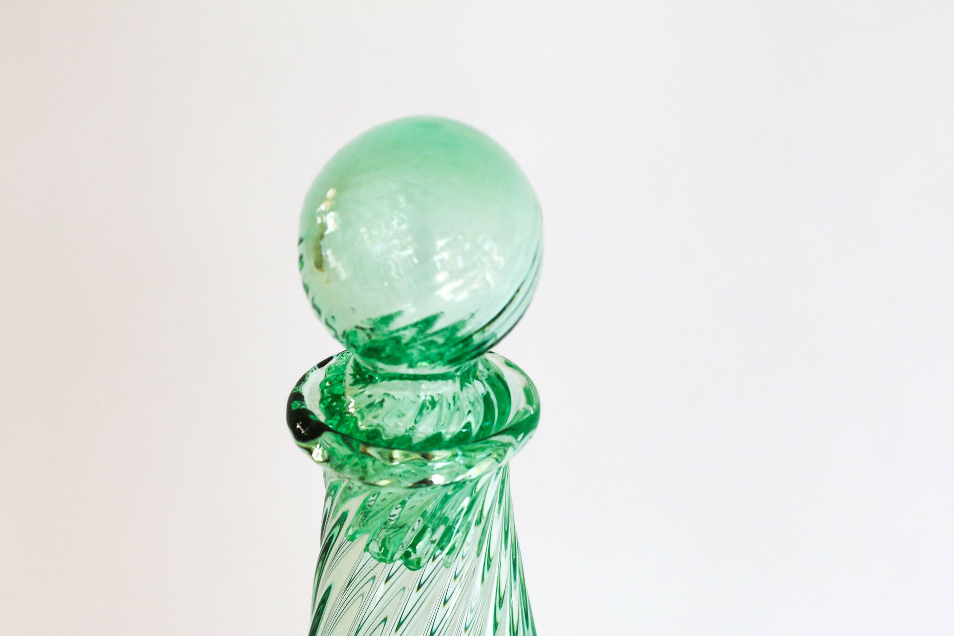 Green glass bottle with a spherical stopper on a light gray background,  available  to buy on the-salon.com. SALON curates the finest , unique, handmade pieces from the interior industry's best makers and brands. Shop luxury furniture, lighting, rugs, art, antiques and vintage pieces and accessories from SALON interior designed rooms.
