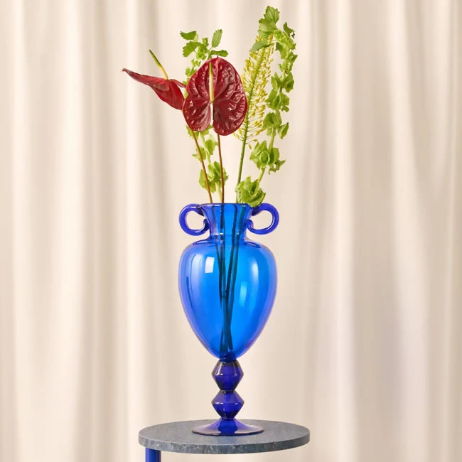 Blue glass vase with floral arrangement on a white background,  available  to buy on the-salon.com. SALON curates the finest , unique, handmade pieces from the interior industry's best makers and brands. Shop luxury furniture, lighting, rugs, art, antiques and vintage pieces and accessories from SALON interior designed rooms.