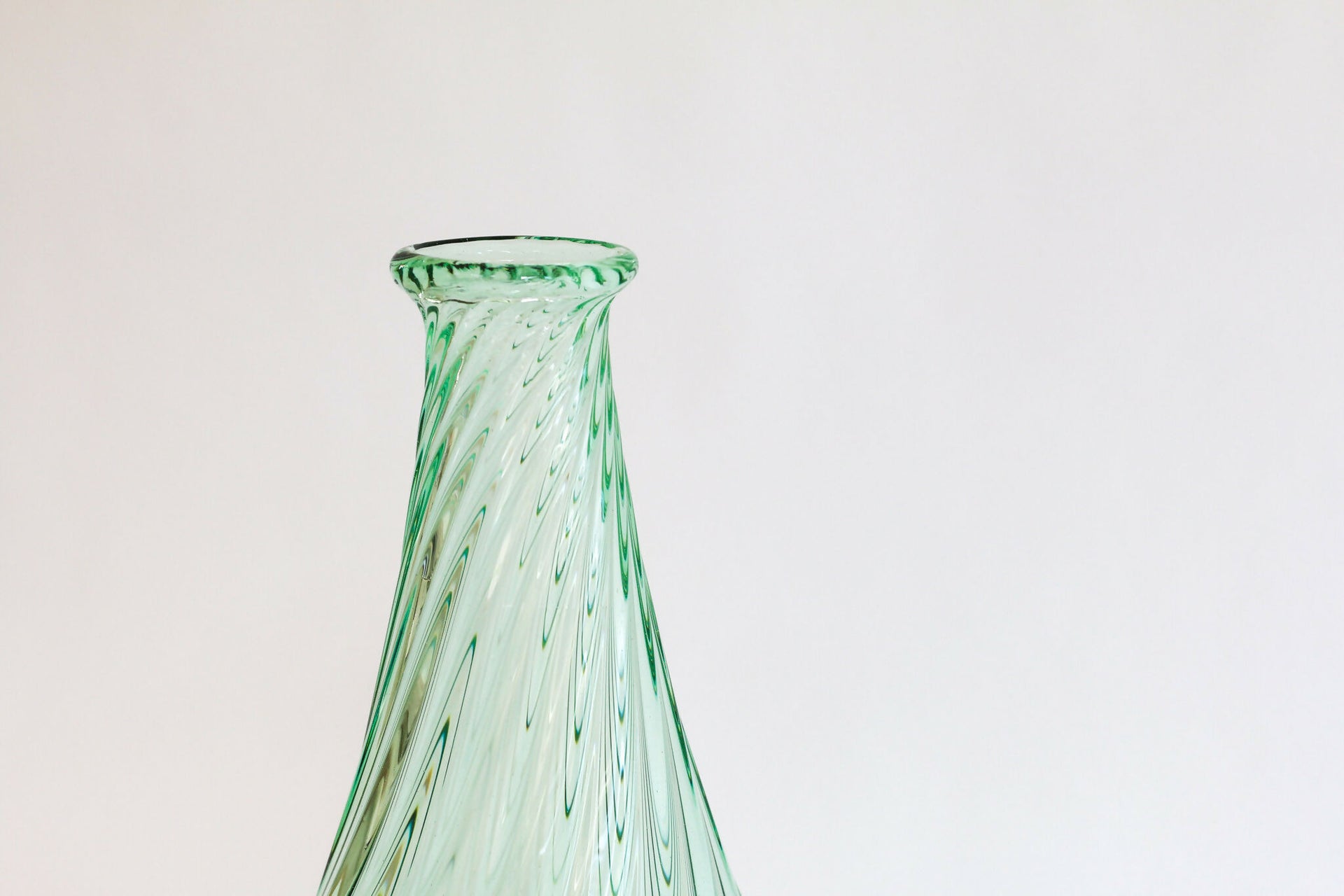 Green glass vase on a light gray background,  available  to buy on the-salon.com. SALON curates the finest , unique, handmade pieces from the interior industry's best makers and brands. Shop luxury furniture, lighting, rugs, art, antiques and vintage pieces and accessories from SALON interior designed rooms.