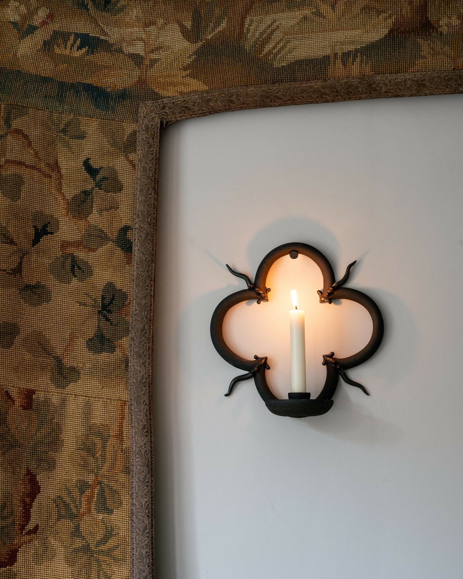 Decorative wall sconce with a candle on a white wall next to patterned wallpaper,  available  to buy on the-salon.com. SALON curates the finest , unique, handmade pieces from the interior industry's best makers and brands. Shop luxury furniture, lighting, rugs, art, antiques and vintage pieces and accessories from SALON interior designed rooms.