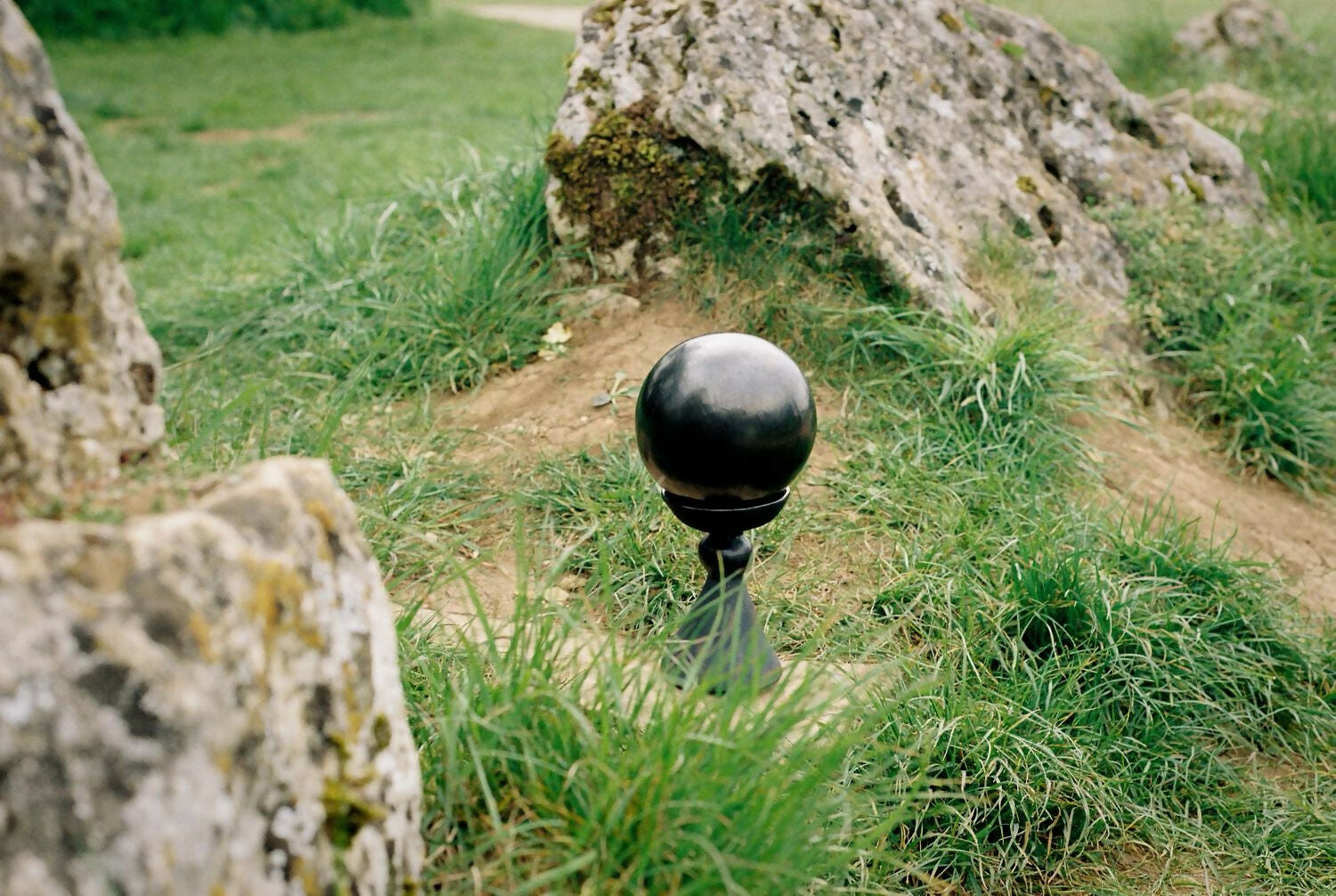 Black spherical object on a grassy path with large stones in the background,  available  to buy on the-salon.com. SALON curates the finest , unique, handmade pieces from the interior industry's best makers and brands. Shop luxury furniture, lighting, rugs, art, antiques and vintage pieces and accessories from SALON interior designed rooms.