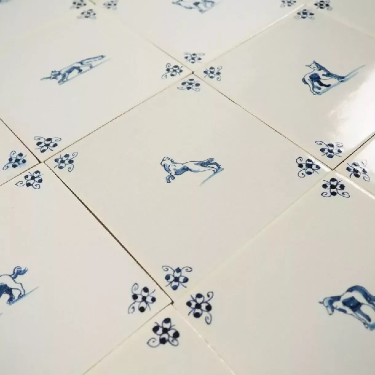 White tiles with blue floral and animal patterns,  available  to buy on the-salon.com. SALON curates the finest , unique, handmade pieces from the interior industry's best makers and brands. Shop luxury furniture, lighting, rugs, art, antiques and vintage pieces and accessories from SALON interior designed rooms.