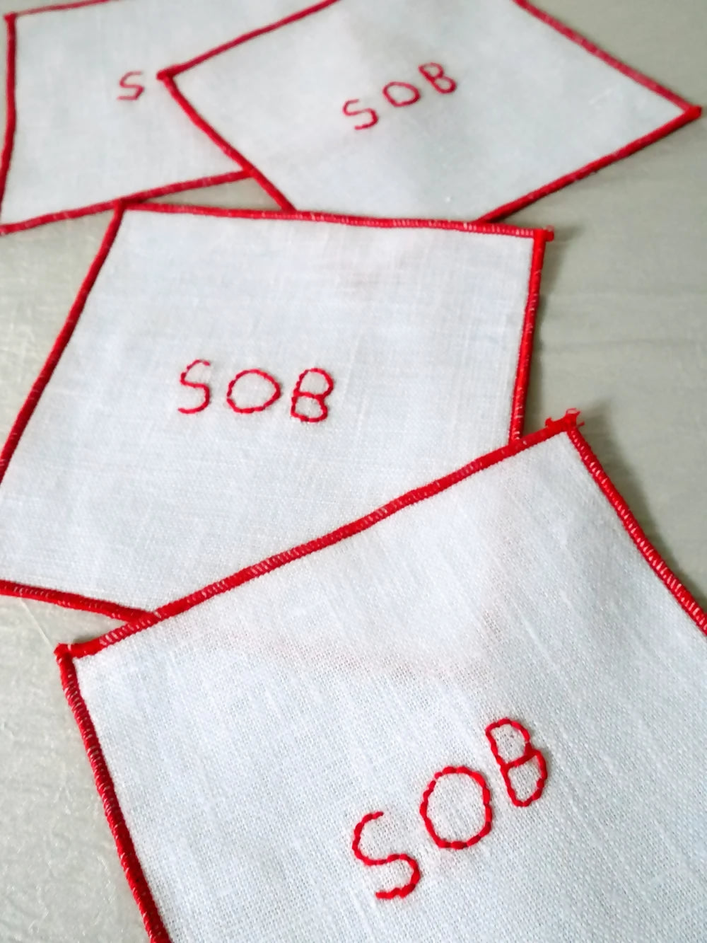 White linen napkins with 'SOB' embroidered in red on a light background, available  to buy on the-salon.com. SALON curates the finest , unique, handmade pieces from the interior industry's best makers and brands. Shop luxury furniture, lighting, rugs, art, antiques and vintage pieces and accessories from SALON interior designed rooms.