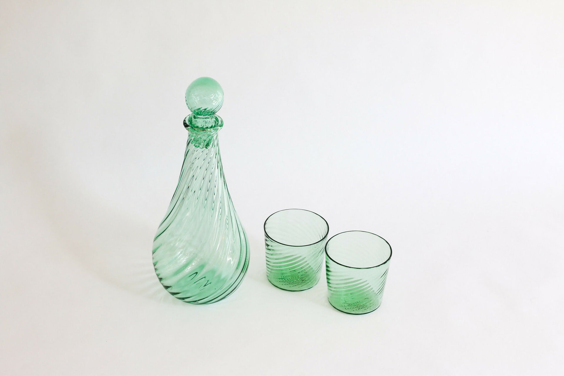 Green glass decanter and two glasses on a white background,  available  to buy on the-salon.com. SALON curates the finest , unique, handmade pieces from the interior industry's best makers and brands. Shop luxury furniture, lighting, rugs, art, antiques and vintage pieces and accessories from SALON interior designed rooms.